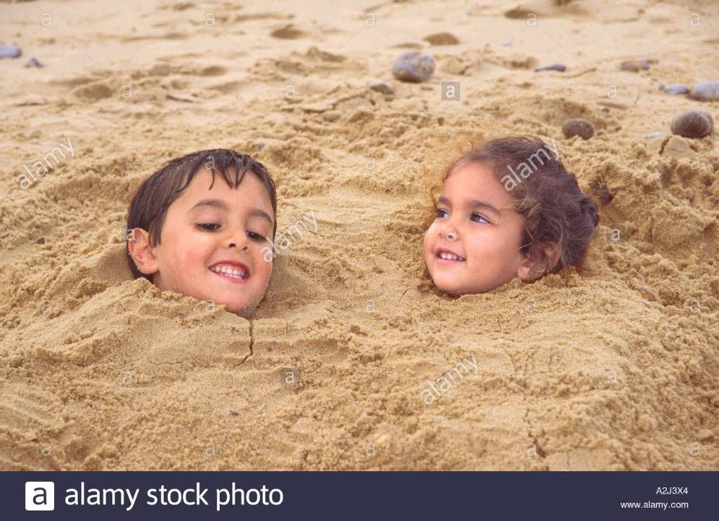 two-young-children-buried-in-sand-on-the-beach-norfolk-A2J3X4.jpg